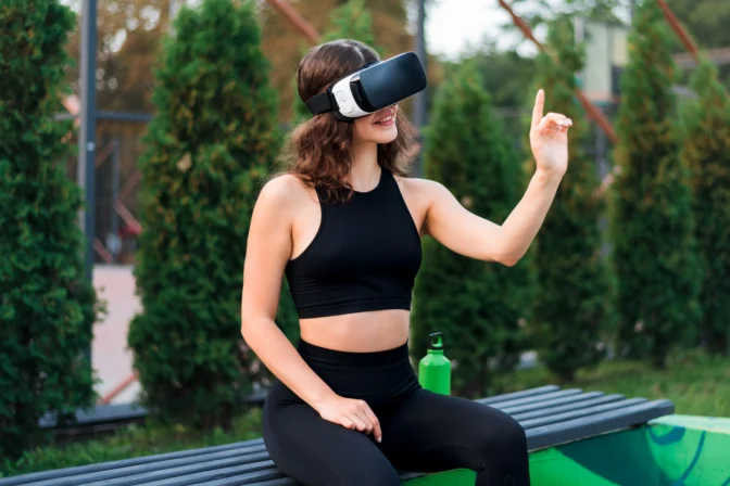smiling-woman-using-vr-headset-tracksuit-while-sitting-bench-sports-field-park (1)